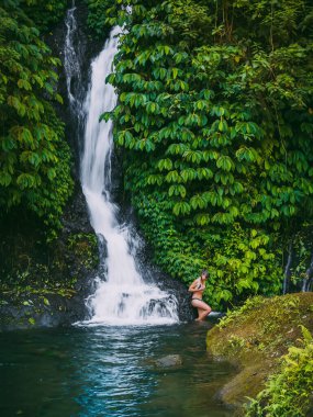 Bali, Endonezya 'da bikinili kadın ve tropikal doğa şelalesi.