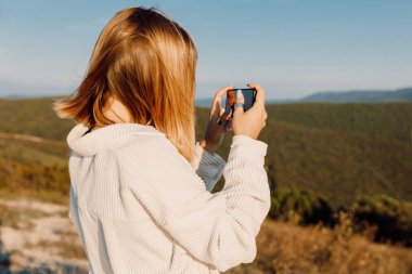 Blonde woman outdoor photography with smartphone. Girl shooting landscapes on smartphone