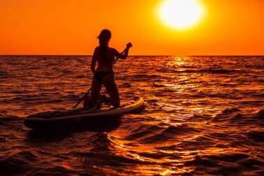 15 Temmuz 2021. Anapa, Rusya. Çekici kadın günbatımında ya da gündoğumunda sakin denizde ayağa kalk. Kırmızı yüzgeçli kadın SUP tahtası ve günbatımı.