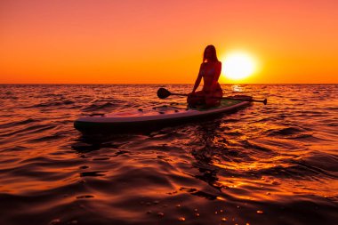 15 Temmuz 2021. Anapa, Rusya. Çekici kadın günbatımında ya da gündoğumunda sakin denizde ayağa kalk. Kırmızı yüzgeçli kadın SUP tahtası ve günbatımı.