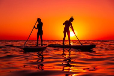 15 Temmuz 2021. Anapa, Rusya. Günbatımında veya gündoğumunda okyanusta kürek çeken gezginlerin silueti. Aile Red Paddle yemek masasında ve günbatımında yansımayla