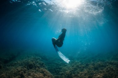 Özgür kadın mavi okyanusta yüzgeçleriyle süzülüyor. Freediver ve güzel güneş ışığı