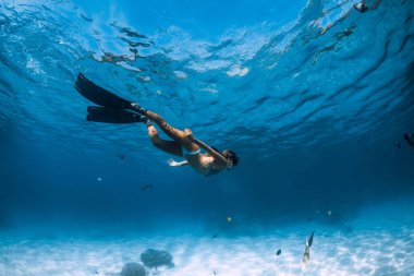 Kadın serbest dalgıç kumlu zeminde yüzgeçlerle suyun altında süzülüyor. Hawaii 'de serbest dalış