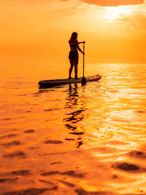 25 Haziran 2021. Anapa, Rusya. Denizde gün batımlı ya da gündoğumlu kürek çeken sporcu bir kadın. Red Paddle yemek masasında bir kadınla yaz günü.