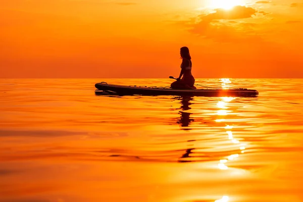 2021年6月25日 ロシアのアナパ スポーティ女性は日没や日の出と静かな海でスタンドアップパドルボードにリラックスします レッドパドルSupボードと日没の女性 — ストック写真