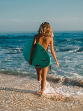 Gün batımında sahilde sörf tahtası olan çıplak sörfçü kadın ya da gün doğumu okyanusa gider.