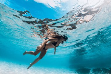 Woman with diving mask swimming underwater in transparent ocean with sandy bottom