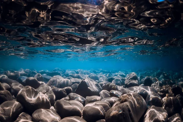 Underwater view with stones bottom and reflection in ocean.