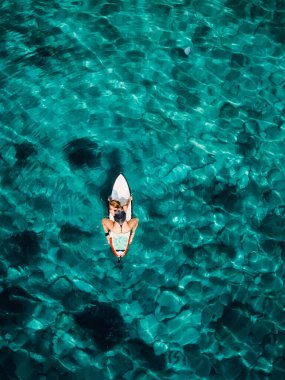 Surf girl sitting on surfboard and wait wave in turquoise ocean. Aerial view with surfer woman