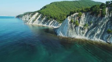 Aerial view of scenic coastline with blue sea and cliffs with pine forest. Summer day on quiet sea