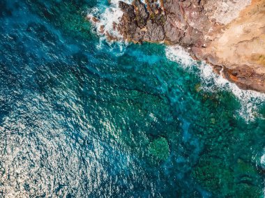 Blue transparent ocean with rocky coastline in sunny day. Aerial view.