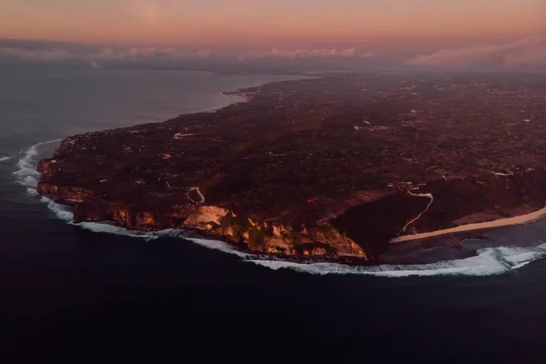 Aerial view of peninsula with cliff and ocean with warm sunset tones in Bali
