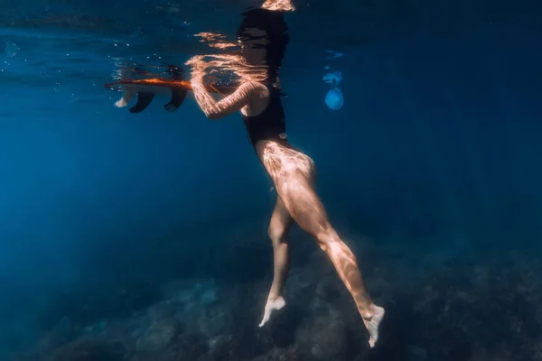 Surfer swimming with board in blue sea. Underwater view with woman and surfboard