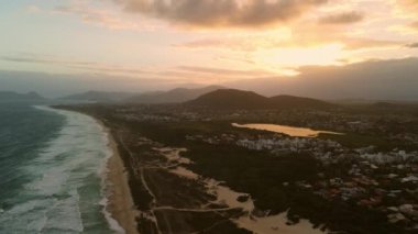 Sandy beach with dunes, ocean and town with sunset lights in Campeche, Florianopolis
