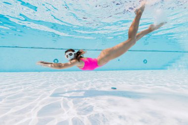 Pembe mayo giymiş çekici bir kadın dalıyor ve havuzda yüzüyor.