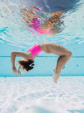 Beautiful woman in pink swimwear with diving mask glides underwater in swimming pool.