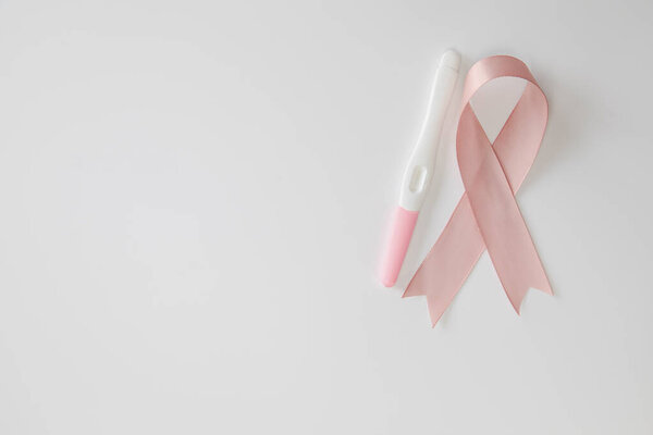 Pink satin breast cancer awareness ribbon with blank pregnancy test isolated on white background top view space for text
