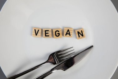 Dining plate with fork and knife with the text VEGAN, concept of dieting vs healthy veganism,vegetarian and healthy lifestyle top view background