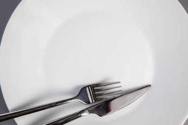 Empty plate with fork and knife on gray background, top view for copy space, food and healthy eating concept space for text