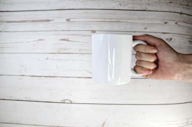Hand holding a ceramic mug blank on wooden background with copy space, space for text