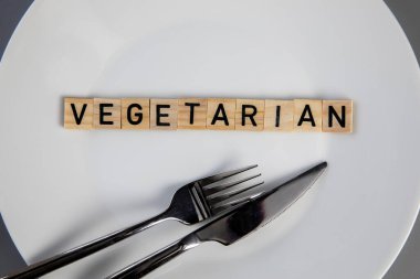 Top view white plate with vegetarian word against grey background top view, knife and fork on table health and food concept close up