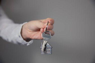 Ev modeli ve anahtarına sahip emlakçı, ev satışı, mülk sahibi ipotek konsepti. Gri arkaplan boşluğunda metin için kopyalama alanı var.
