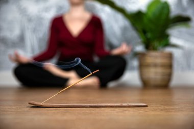 Düşünceli bir kadın elinde tütsü çubuklarıyla evde meditasyon yapıyor, nilüfer çiçeği pozisyonunda oturuyor. Avuçlar yukarı bakacak şekilde el ele tutuşuyorlar. Dikkatli sağlık kavramı