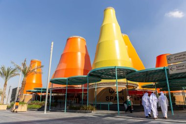 Dubai, BAE, 27.10.2021. 2020 Dubai Fuarı 'ndaki İspanya Ulusal Pavyonu' nda turuncu ve sarı kuleler ve kanduras 'taki adamlar binaya giriyor..