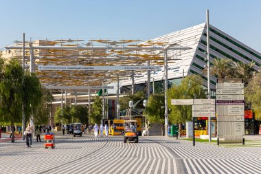 Dubai, BAE, 27.10.2021. Fuar 2020 Dubai, kuş şekilli güneşlik çatısı olan patika, yürüyen insanlar, elektrikli arabalar ve arka planda Suudi Arabistan Pavyonu.