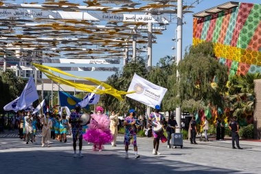 Dubai, BAE, 09.12.2021. Fuar 2020 Dubai Günlük Geçit Töreni ve Palau Ulusal Günü geçit töreni. Renkli Fuar 2020 temalı giysileri ve bayrakları olan insanlar müzik çalıyor ve kutlama yapıyorlar..