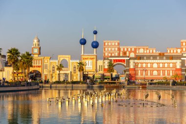 Dubai, BAE, 10.01.21. Bahreyn, Kuveyt ve Yemen ulusal pavyonları ile Dubai 'deki Küresel Köy eğlence parkının peyzajı fıskiye tesisleriyle birlikte pürüzsüz su havuzuna yansıyor..