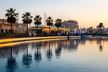 Dubai, BAE, 10.01.21. Gün batımında Dubai 'deki Küresel Köy eğlence parkının arka planında pürüzsüz sulara yansıyan palmiye ağaçları ve Filistin ve Ürdün Pavyonları bulunuyor..