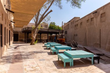 Dubai, BAE, 27.09.2021. Geleneksel Arap tarzı binalar, turkuaz masalar, ahşap geleneksel tekne (dhow) ve güneş gözlükleriyle Al Fahidi Tarihi Taştan Sokak, Deira.
