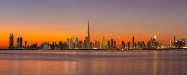 Dubai Ticaret Koyu 'nun panoraması, gün batımından sonra gökyüzü renkli aydınlık binalar ve sakin Dubai Deresi suyuyla kaplanır..