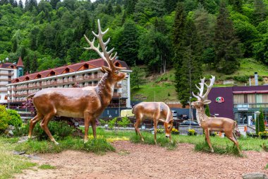Sairme, Georgia, 06.06.21. Artificial deers statues, decoration in health resort Sairme in Lesser Caucasus mounatins with Sairme Hotel building and lush green forest in the background.