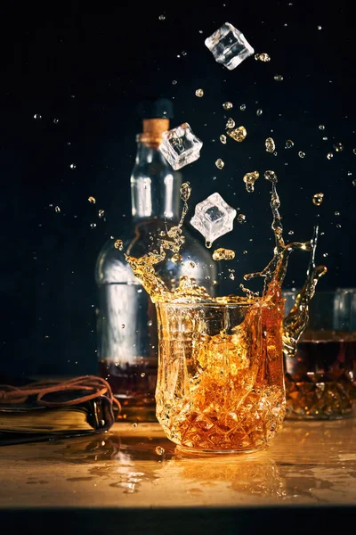 Ice falls into a glass of cognac — Stock Photo, Image