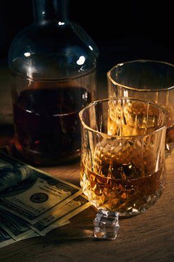 İki bardak buzlu rom, birkaç dolar ve arka planda bir şişe de ahşap masa.