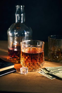 İki bardak buzlu rom, birkaç dolar ve arka planda bir şişe de ahşap masa.