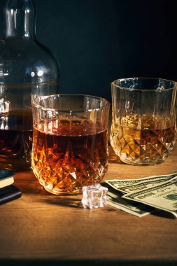 İki bardak buzlu rom, birkaç dolar ve arka planda bir şişe de ahşap masa.