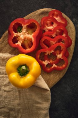 Koyu bir arka planda tahta kesme tahtasındaki sarı ve kırmızı biberler