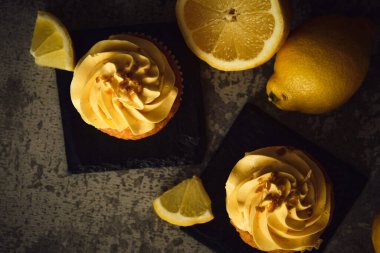 Koyu arkaplanda sarı limon dilimlerinin yanında iki limonlu kek.