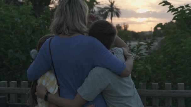 橋の上に2人の子供を持つ若い女性が夕日を見て抱擁し — ストック動画