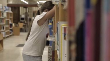 Bir kız kütüphanede kitaplara bakıyor.