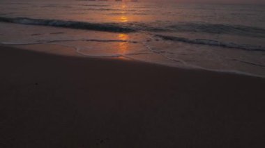 Güneşin yol açtığı sakin dalgalarla kumsalda erken güzel bir gün doğumu