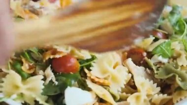 mixing with a wooden spatula ready-made salad of colored pasta