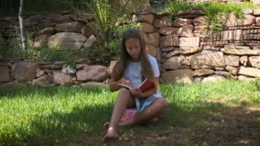 a girl is sitting on the grass in the garden with a book