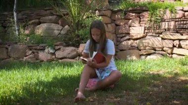 a girl is sitting on the grass in the garden with a book