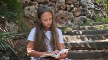 a girl with a book is sitting on the wooden steps in the garden