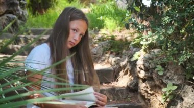 a girl with a book is sitting on the wooden steps in the garden