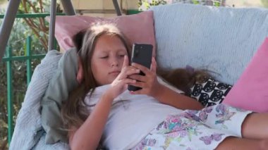 a girl is sitting on the terrace playing games on a gadget